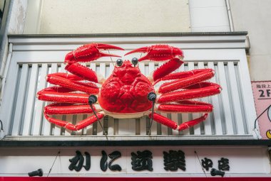 Osaka, JAPAN - CIRCA 29 Aralık 2023: Dotonburi caddesinde turistlerin gelip tadını çıkarmaları için kral yengeci şeklinde yürüyen Japon restoranının işaretleri.