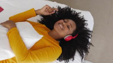 Afrika kökenli Amerikalı genç bir kadının yatakta dinlenip kulaklıkla müzik dinlemesinin en iyi görüntüsü..