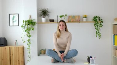 Nilüfer çiçekli gülümseyen genç iş kadını ofis masasında oturuyor. Gözü kapalı mutlu bir girişimci zihinsel denge için meditasyon yapıyor.