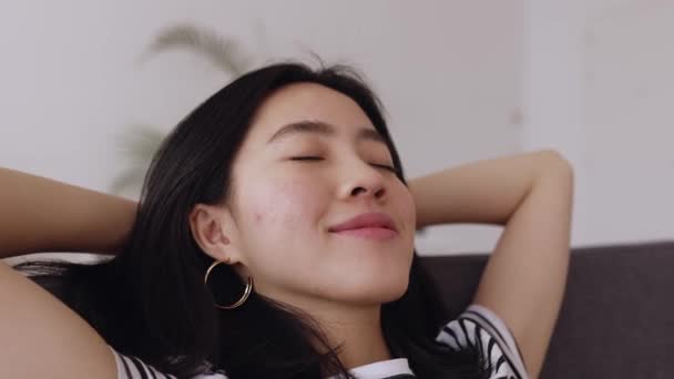 自宅のソファでリラックスした頭の後ろに手を持つ若い中国人女性 Joyful Chinese Ethnicity Female Daydreaming Couch — ストック動画