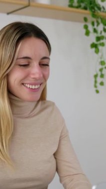 Ev ofisinden dizüstü bilgisayarla çalışan mutlu genç bir kadının dikey görüntüleri. İş kadını girişimci masa başında oturmuş bilgisayarda yazı yazıyor.