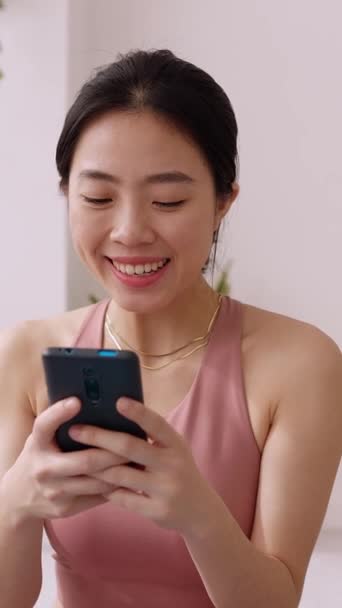 運動ルーチン後の携帯電話を使用して若いアジアの女性の垂直ショット 中国のフィットネス女性は自宅で運動中に携帯電話でリラックス スローモーション高品質4K映像 — ストック動画