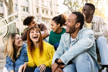 Latin kökenli bir grup genç arkadaş dışarıda eğleniyor. Millennial çok ırklı insanlar gülerken sosyal toplantı şehrin merdivenlerinde oturuyor.