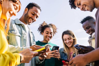 Dışarıda akıllı cep telefonu kullanan bir grup mutlu genç arkadaş. Çok ırklı gençler cep telefonu uygulamasında sosyal medya içeriğini paylaşarak birlikte eğleniyorlar. Teknoloji yaşam tarzı konsepti