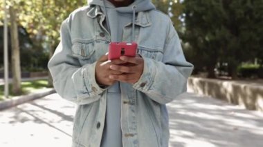 Gülümseyen Afrikalı Amerikalı genç bir kadının şehir parkında yürürken cep telefonu kullanmasına ön görüş - gençlik, sosyal medya ve milenyum insanları kavramı. Yüksek kaliteli FullHD görüntüler