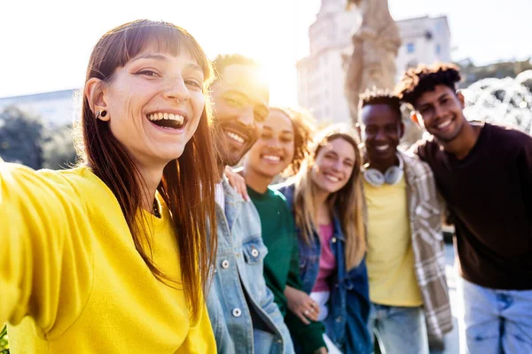 Smiling millennial friends having fun taking selfie portrait together outside. Diverse teenage people looking at camera standing in line for photo group. Multiracial friendship concept