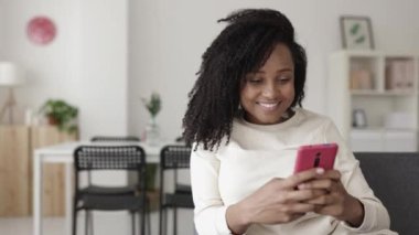 Evdeki koltukta rahatlarken cep telefonu kullanan mutlu genç bir kadın. Yüksek kalite 4k görüntü