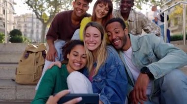 Mutlu genç bir grup insan seyahat tatillerinde dışarıda otururken selfie çektirirken eğleniyor. Çok ırklı dostluk ve tatil kavramı