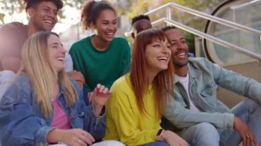 Latin kökenli bir grup genç arkadaş dışarıda eğleniyor. Millennial çok ırklı insanlar gülerken sosyal toplantı şehrin merdivenlerinde oturuyor.