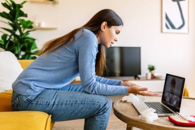 Genç bir kadın laptoptaki tıbbi danışmanlık yoluyla doktorla konuşuyor.