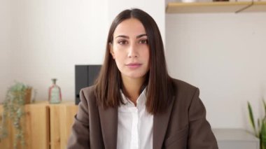 Masada oturan ciddi iş kadınının kendine güvenen video portresi. Kameraya bakan güzel bir bayan girişimcinin ön manzara portresi. Başarılı insanlar konsepti