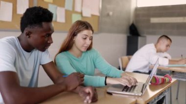 Lisede laptopta çalışan iki çok ırklı öğrenci arkadaş. Sınıfta okuyan çok ırklı genç sınıf arkadaşları. Takım çalışması ve eğitim kavramı