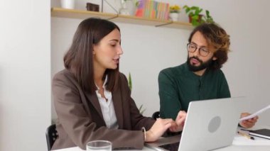 Dizüstü bilgisayarda çalışan genç bir iş kadını iş yerinde oturan bir meslektaşla projeyi tartışıyor. Takım çalışması ve beyin fırtınası konsepti