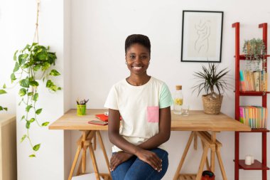 Evdeki işyerinde oturan neşeli, modaya uyan yaratıcı kadının portresi.