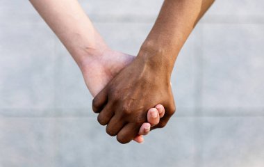 İki farklı kadının el ele tutuşup birlik ve destek verdiği yakın çekim. Tanımlanamayan Afrikalı ve Kafkasyalı kadınların birbirini tuttuğu topluluk ve çeşitlilik kavramı