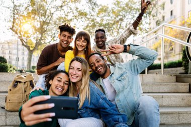 Multiracial young happy group of student friends taking selfie portrait together using mobile phone outdoors