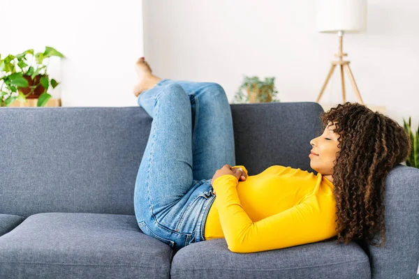 Young woman relaxing on sofa at home. African american female sleeping on couch in the living room