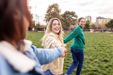 Three young multiracial female friends having fun running holding hands together outdoor. Female friendship lifestyle