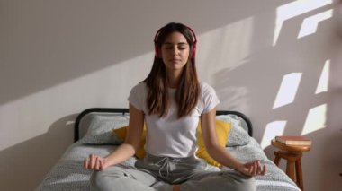 Genç, güzel bir kadın kulaklıkla nefes alıyor. Yatakta meditasyon yapıyor. Rahatlamak için müzik dinliyor ya da yoga yaparken podcast yapıyor.. 