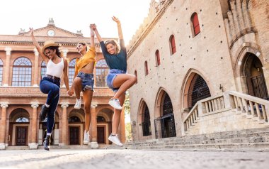 Three young happy women enjoying summer holidays. Millennial female having fun jumping together at old town city street. Vacation lifestyle and friendship concept