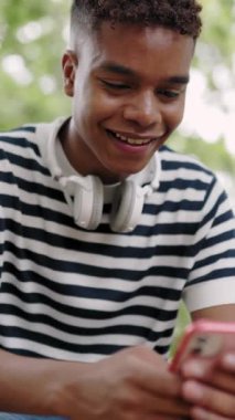 Vertical HD shot footage of young latin american teenage boy using mobile phone outside. Millennial student man chatting on smartphone app. Technology lifestyle concept.