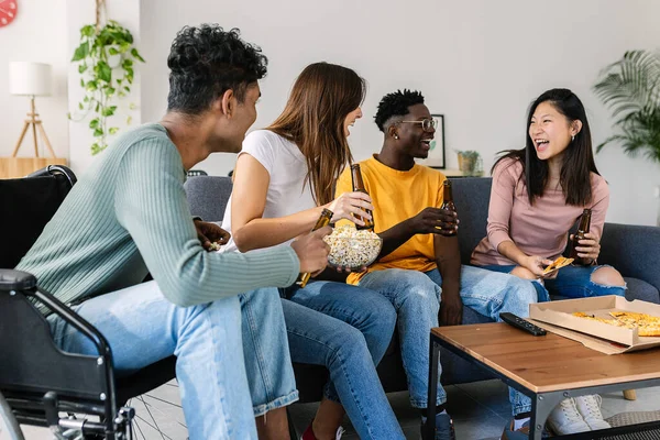 Group of multiracial friends social gathering at home. Disabled young indian man having fun with multiracial teenage friends eating pizza at home. Inclusion and diversity concept