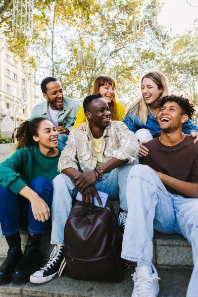 stock image Vertical shot of happy multi-ethnic group of young hipster diverse student friends having fun together while hanging out sitting together outdoors. Friendship concept