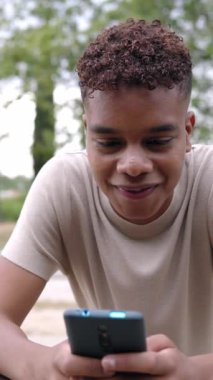 Vertical video footage of smiling young adult hispanic american man using smart mobile phone outdoor.Latin millennial student chatting with friends on cellphone app. 