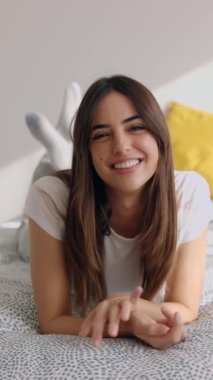 Vertical video portrait of happy pretty young woman smiling at camera while relaxing on bed. Beautiful and cheerful people concept