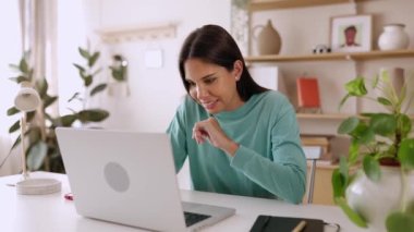 Ev ofisinde dizüstü bilgisayarla çalışan mutlu genç bir kadın. Milenyum kız öğrencileri online olarak oturma odasında masa başında oturarak öğreniyor. Eğitim ve Serbest Çalışanlar Konsepti