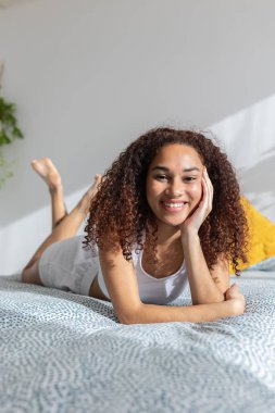Vertical portrait of smiling young latin american woman relaxing on bed in the morning