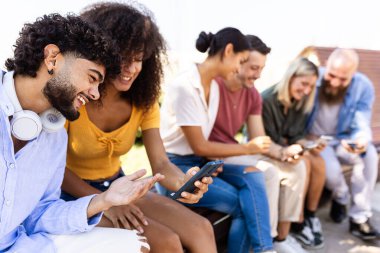 Mutlu genç öğrenci arkadaş grubu akıllı cep telefonu uygulamasından sosyal medya içeriğini izlerken birlikte eğleniyor.