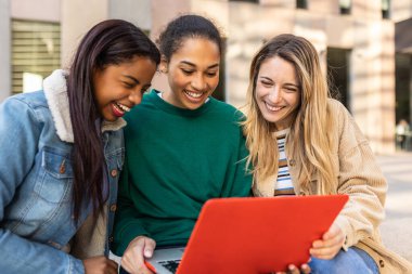 Üç genç milenyum öğrencisi dışarıda dizüstü bilgisayarda birlikte çalışıyorlar. Eğitim ve takım çalışması kavramı