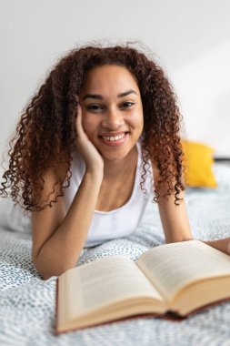 Yatakta kitap okuyan Latin Amerikalı kadının dikey portresi. Boş zaman, edebiyat ve insan konsepti