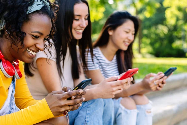 stock image Three joyful multiracial young teenage girls having fun together outdoors. Addicted millennial female watching social media content on smart phone device app. Technology lifestyle concept