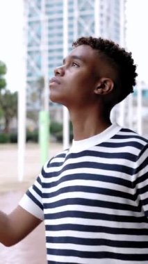 Verandanın altındaki yağmurdan korunan şemsiyesiz genç bir adamın dikey video görüntüleri. Milenyum çocuğu yağmurlu bir günde yağmur yağıyor mu diye kontrol ediyor.