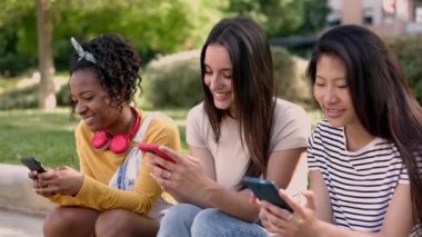 Mutlu, genç, çok ırklı kadın arkadaşlar sokakta cep telefonu kullanırken eğleniyorlar. Akıllı telefon uygulamasında komik sosyal medya içeriğini izlerken üç farklı kadın birlikte gülüyor.