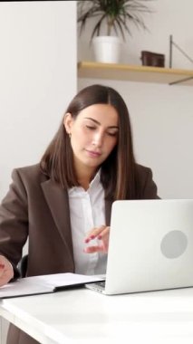 İş yerinde laptopta çalışan genç ve güzel bir iş kadınının dikey videosu. Ofiste yeni başlatılan proje üzerinde çalışan başarılı profesyonel kadın..