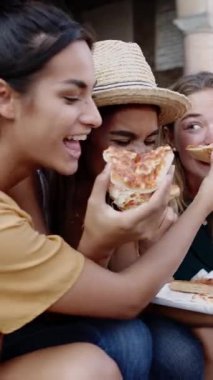 İtalya 'da yaz tatilinde sokakta pizza yiyen üç çok ırklı kadının dikey çekimi. Gençlerin yaşam tarzı ve kadın arkadaşlığı kavramı