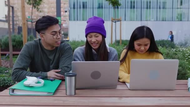 三位带着笔记本电脑的年轻的亚洲学生朋友坐在大学校园的桌子上一起工作 团队合作 大学生活方式和人的概念 — 图库视频影像
