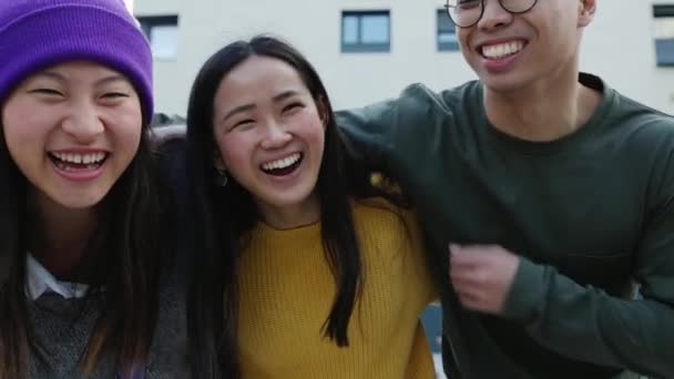 一群年轻的亚洲朋友在户外互相拥抱大笑 三个同族同学在市区街上玩得很开心 — 图库视频影像