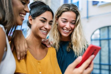 Şehir caddesinde cep telefonu kullanan üç farklı genç kadın. Cep telefonu uygulamasından sosyal medya içeriğini izleyen güzel yüzlü kadınlar. Bağlı insanlar ve arkadaşlık kavramı