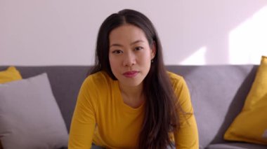 Evdeki kanepede kameraya gülümseyen neşeli Asyalı kadın. Bin yıllık Çinli bir kadının pozitif yüz portresi. Mutlu insanlar konsepti.