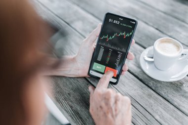Şifreli para satmak için cep telefonu uygulaması kullanan bir kadının omuzlarının üstünden. Dijital yaşlılar ve borsa konsepti