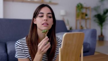 Happy young woman using natural rose quartz face roller on cheek