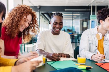 Çok ırklı bir grup üniversite öğrencisi ev ödevi yapıyor ya da kampüs kafeteryasında birlikte oturarak sınav hazırlıyorlar. Takım çalışması ve eğitim yaşam tarzı konsepti.