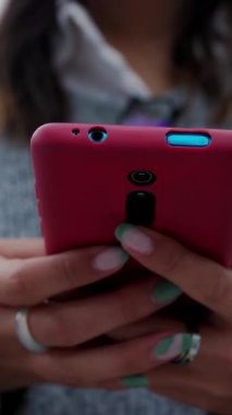 Şehir caddesinde cep telefonuyla gülen mutlu, genç Asyalı kadının dikey görüntüsü. Milenyum kadını akıllı telefon ekranına bakıyor ve yayın platformunda sosyal medya içeriğinin keyfini çıkarıyor.