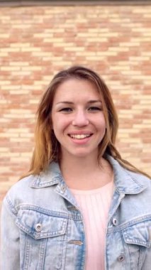 Duvarın üzerinden kameraya gülümseyen güzel sarışın genç bir kadının dikey portresi. Mutluluk ve mutlu insanlar konsepti.