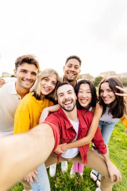 Parkta telefonla selfie çeken çok ırklı genç arkadaşların dikey grup portresi. Milenyum öğrencileri izin gününün tadını çıkarıyor.