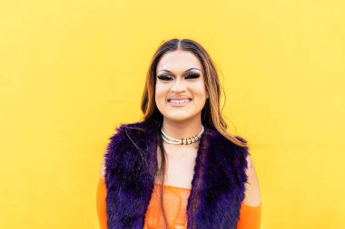 İzole edilmiş LGBTQ genç travesti sarı arka planda kameraya gülümsüyor..